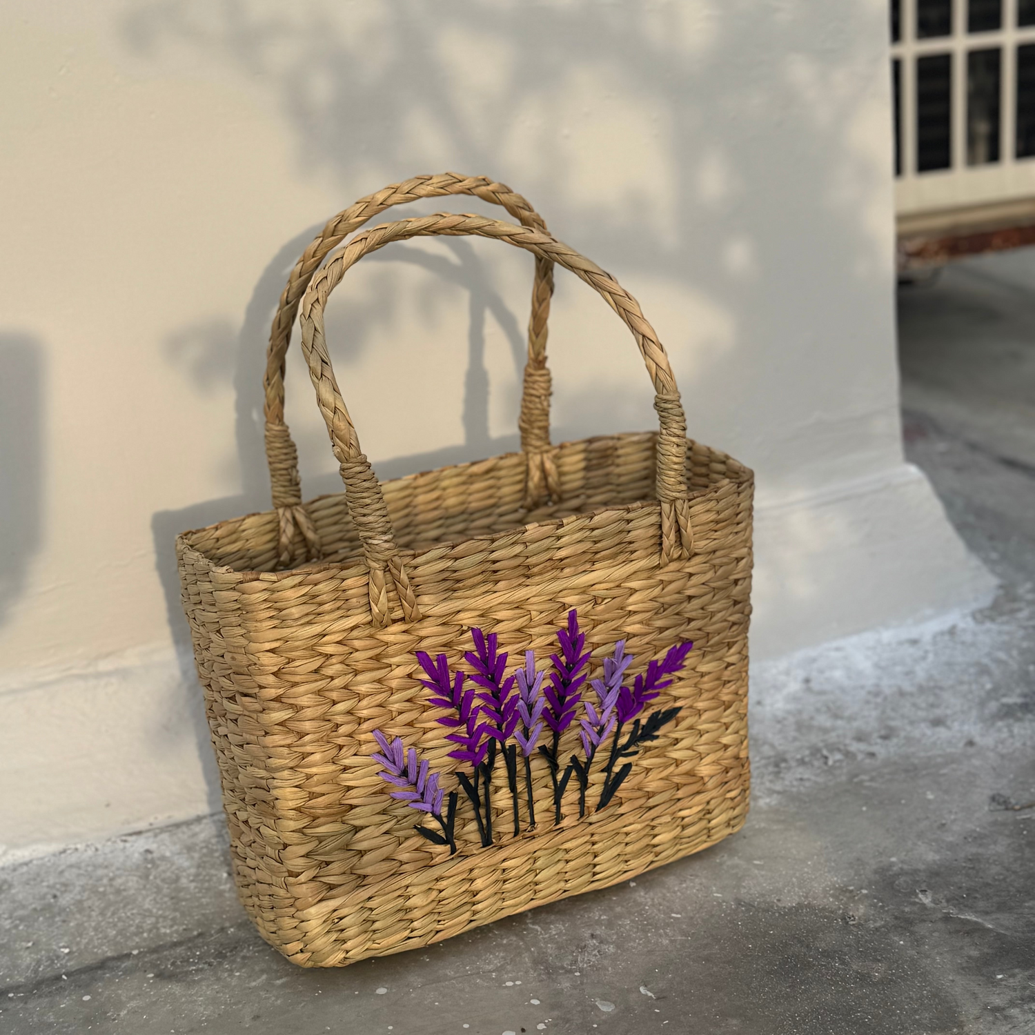Woven basket with embroidered lavender design on a concrete floor.